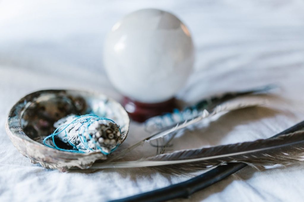 white-and-blue-egg-on-white-and-blue-textile-6806380 A spiritual arrangement featuring a crystal ball, sage bundle, and feathers, ideal for mystical themes.